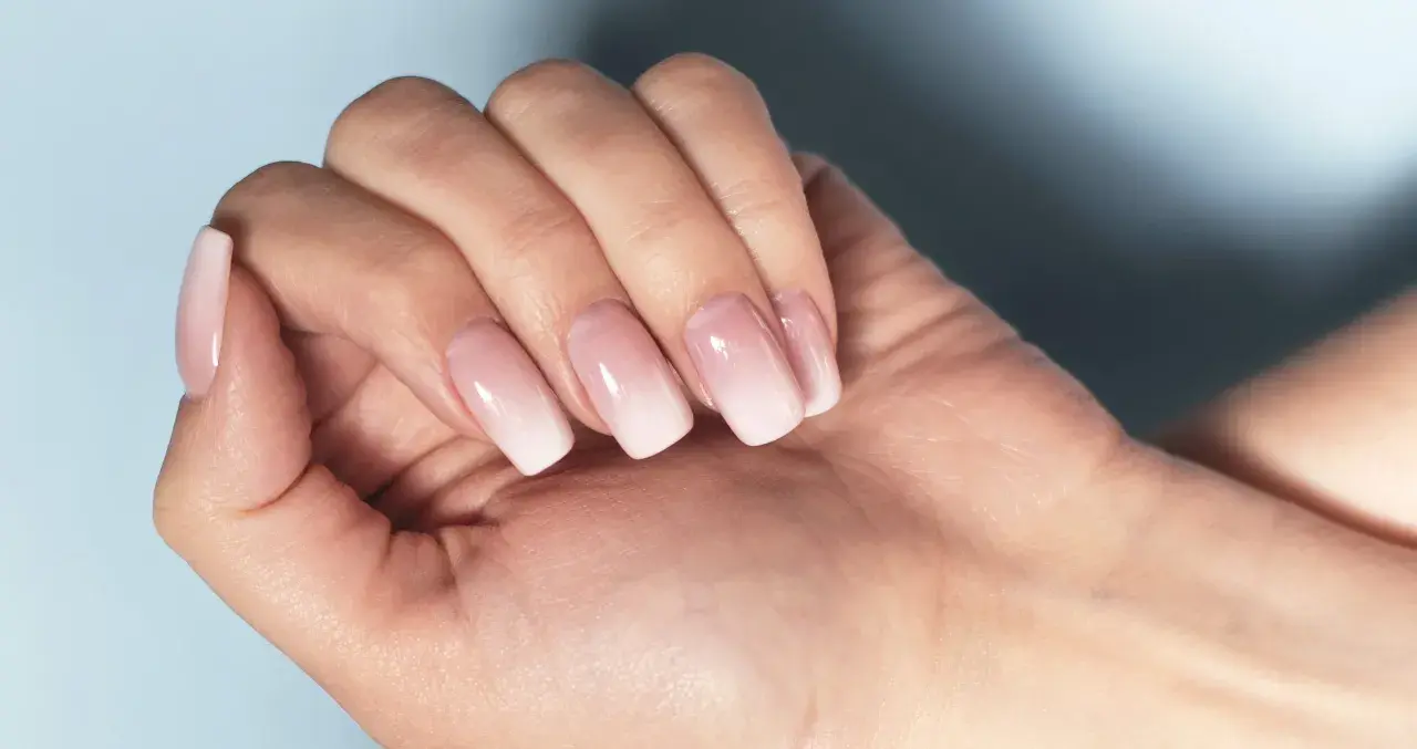 Dłoń z paznokciami w stylu francuski manicure, z delikatnym ombre od różu do bieli.