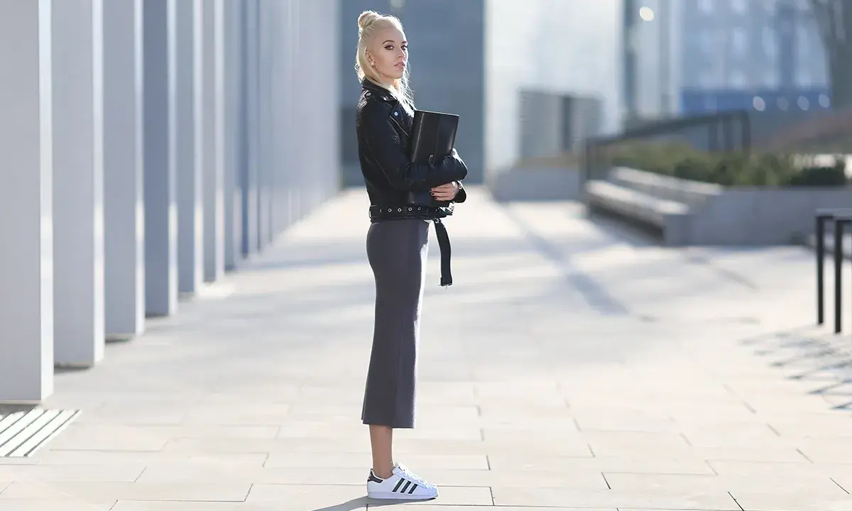 Kobieta w czarnej ramonesce i szarej spódnicy prezentuje stylowe adidas superstar stylizacje na tle nowoczesnej architektury.
