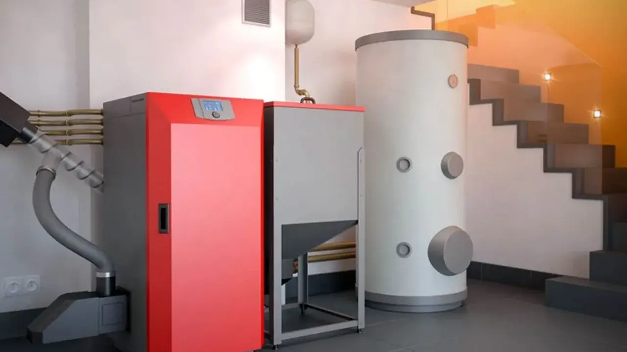 Moderna caldera de pellets roja y gris junto a un gran acumulador de agua. Una solución eficiente para cambiar caldera de gas por pellets.