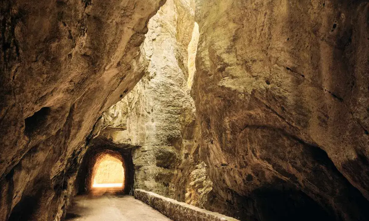 La strada della forra si snoda tra imponenti pareti rocciose, con un tunnel che si apre verso una luce accecante.