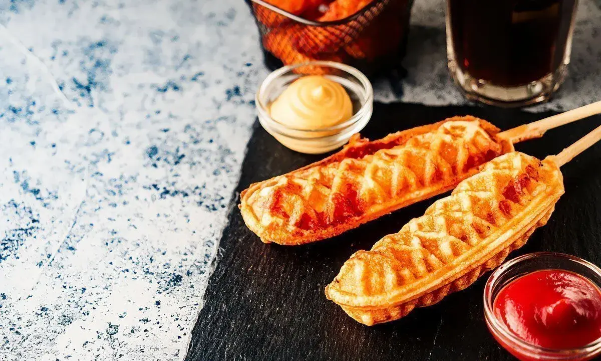 Pyszny corn dog przepis na patyku, podany z ketchupem i musztardą. Idealna przekąska!