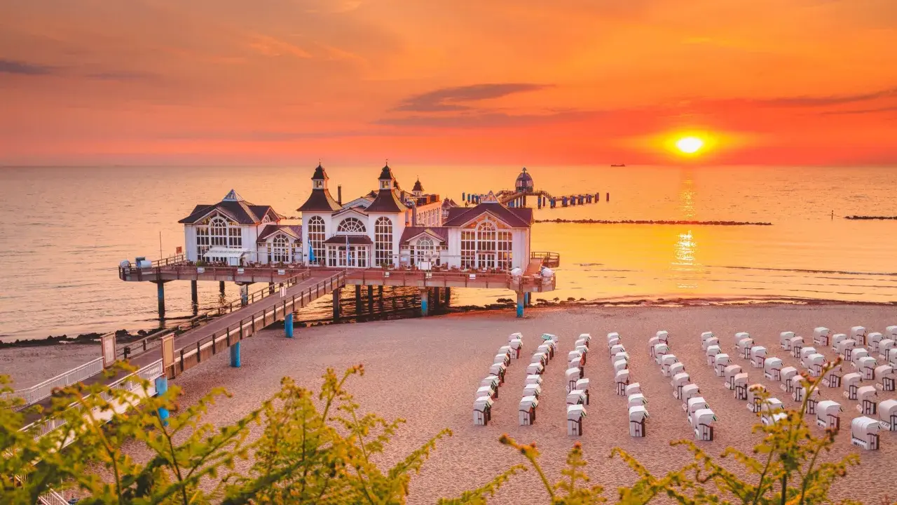 Zachód słońca nad molo w Sellin, na Rugii, największej wyspie Niemiec. Puste kosze plażowe czekają na gości.