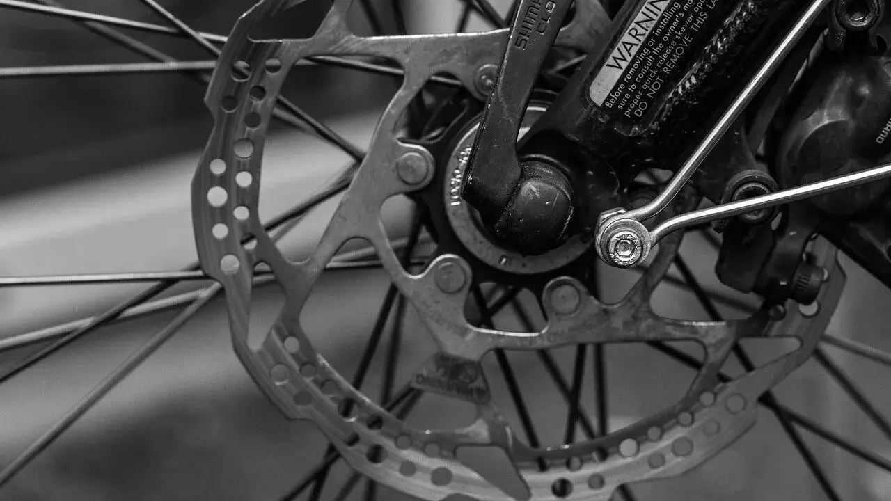 Zbliżenie na tarczę hamulcową i piastę roweru. Widoczne są szprychy, zacisk hamulcowy i dźwignia Shimano. To kluczowe elementy wpływające na przełożenia w rowerze.