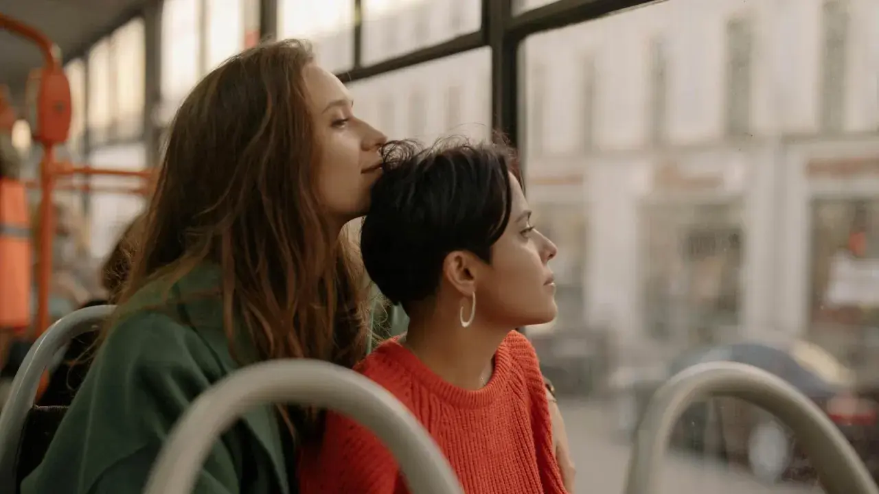 Two women share a tender moment on a bus, perhaps on their gay honeymoon, gazing out the window at the passing scenery.