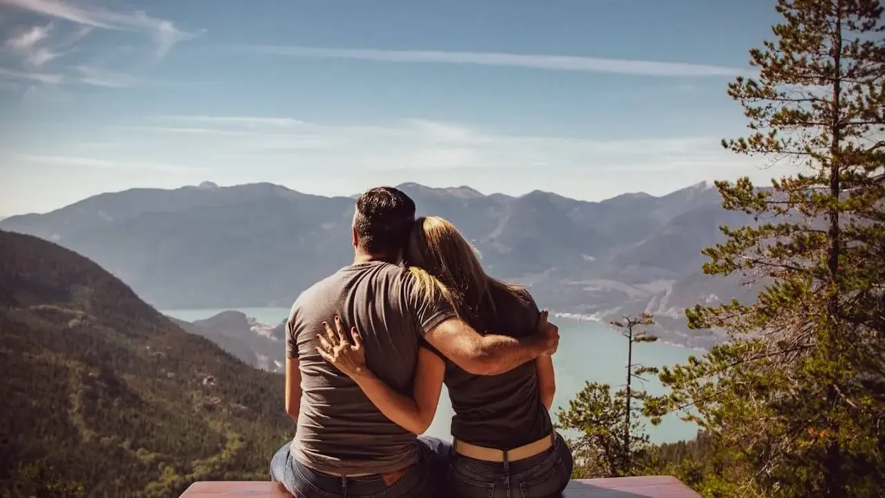 Un couple partage un moment d'amour sensuel, bras dessus, bras dessous, contemplant un paysage montagneux et un lac paisible.