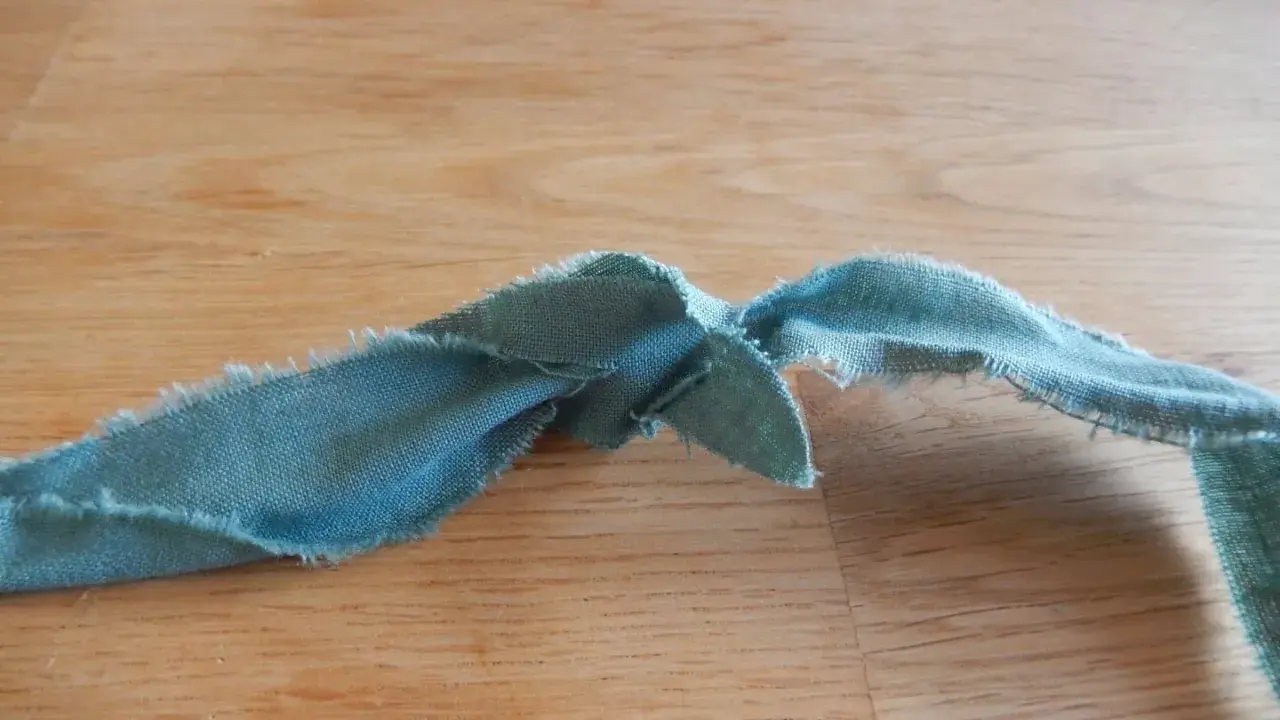 En bit tygremsa, redo att sy ihop trasmattor. Trådar hänger löst från kanterna.