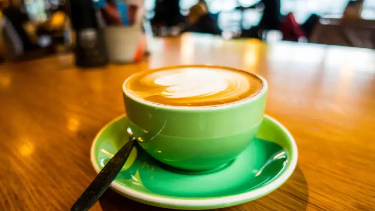 Ein cremiger Cappuccino mit doppeltem Espresso, kunstvoll verziert, in einer leuchtend grünen Tasse auf einem Holztisch.