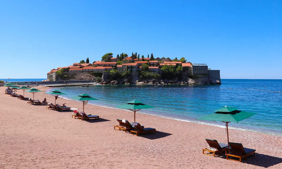 Ein idyllischer montenegro sandstrand mit Liegestühlen und Sonnenschirmen, im Hintergrund die malerische Insel Sveti Stefan.