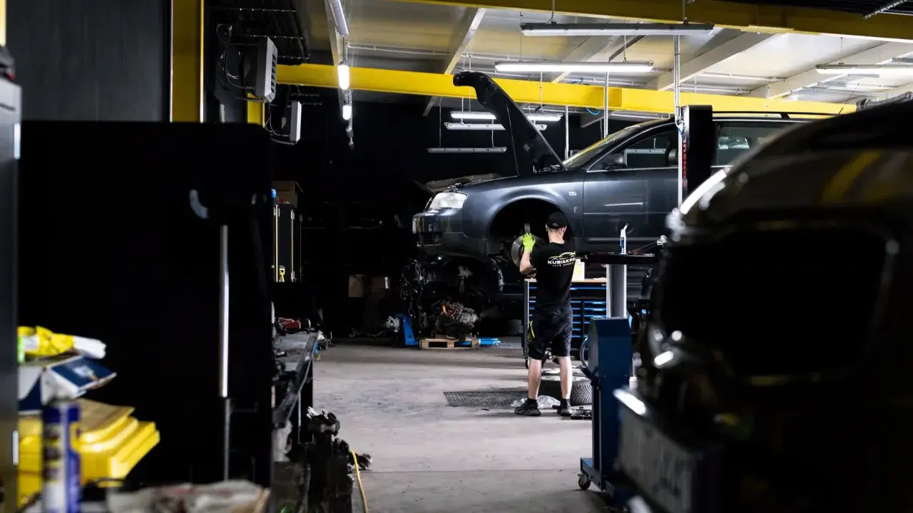 Mechanik bada przyczynę, dlaczego auto nie odpala. Podniesiony przód pojazdu i widoczny silnik sugerują skomplikowaną usterkę.