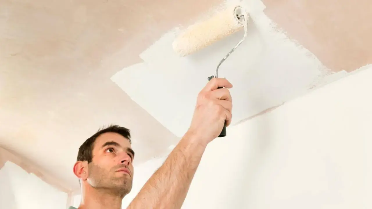 Hombre pintando el techo con rodillo. Se ve la mano sujetando el rodillo y la pintura blanca aplicándose.