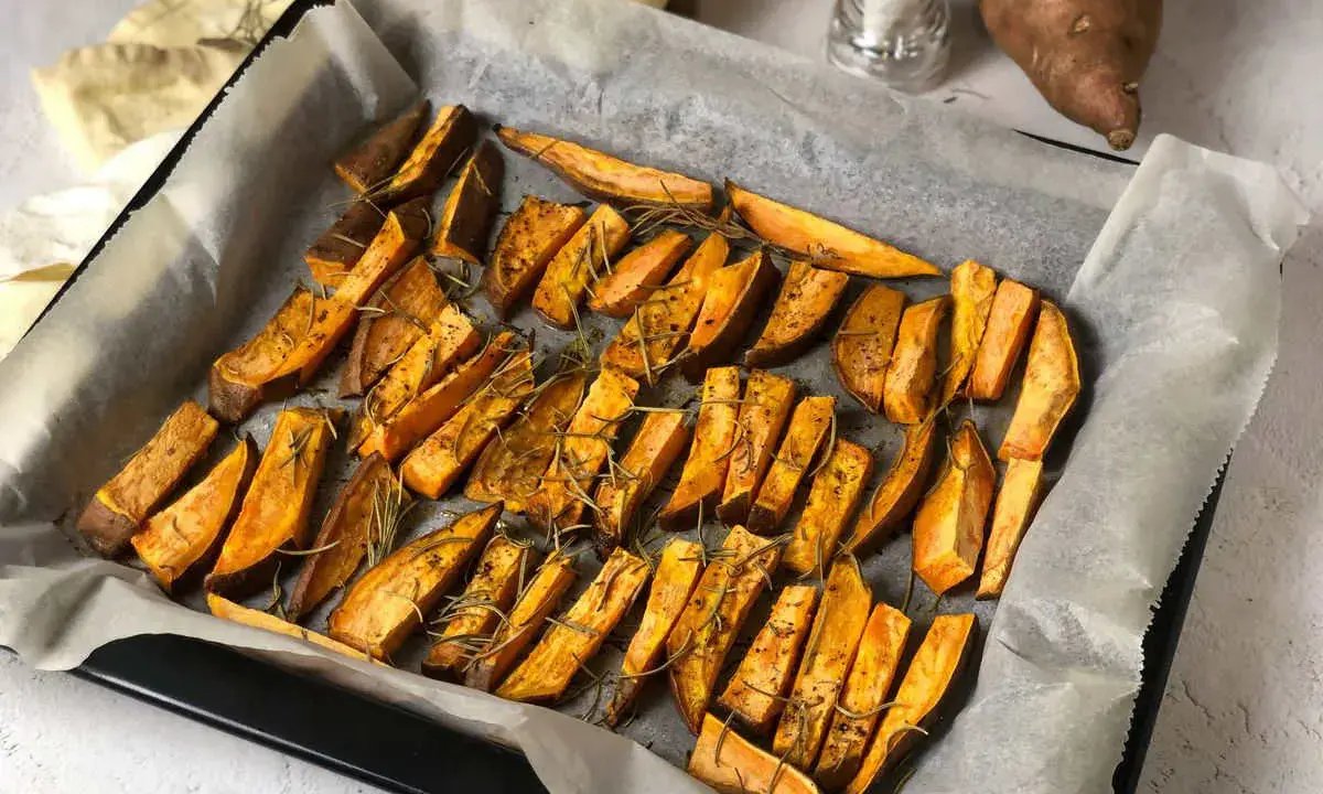 Patate dolci al forno tagliate a spicchi, condite con rosmarino e spezie, pronte per essere gustate.