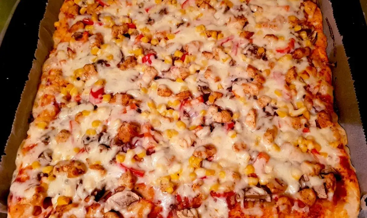 Pyszne, prostokątne ciasto na pizzę z suchych drożdży, obficie posypane kurczakiem, kukurydzą i serem.