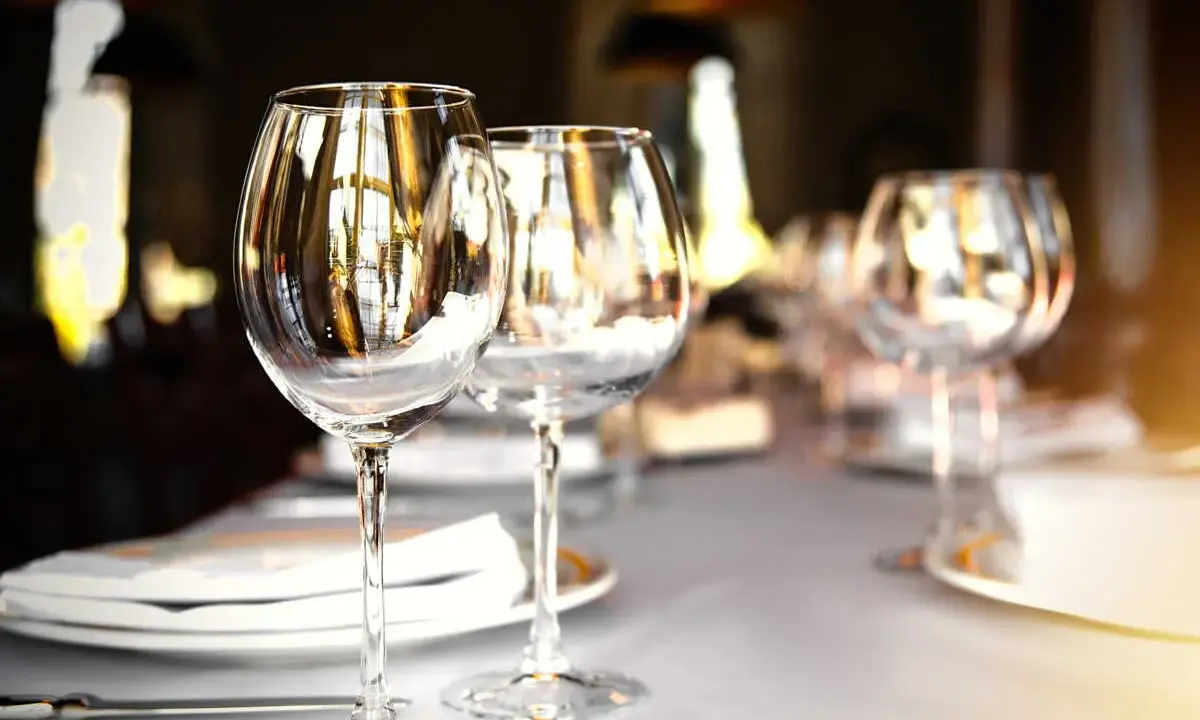 Verres à vin vides sur une table dressée, prêts pour un repas. L'emplacement verre table est soigné, reflétant la lumière ambiante.