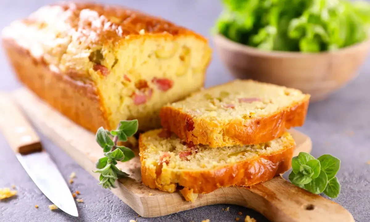 Tranche de cake jambon fromage dorée, garnie d'herbes fraîches, prête à être dégustée.