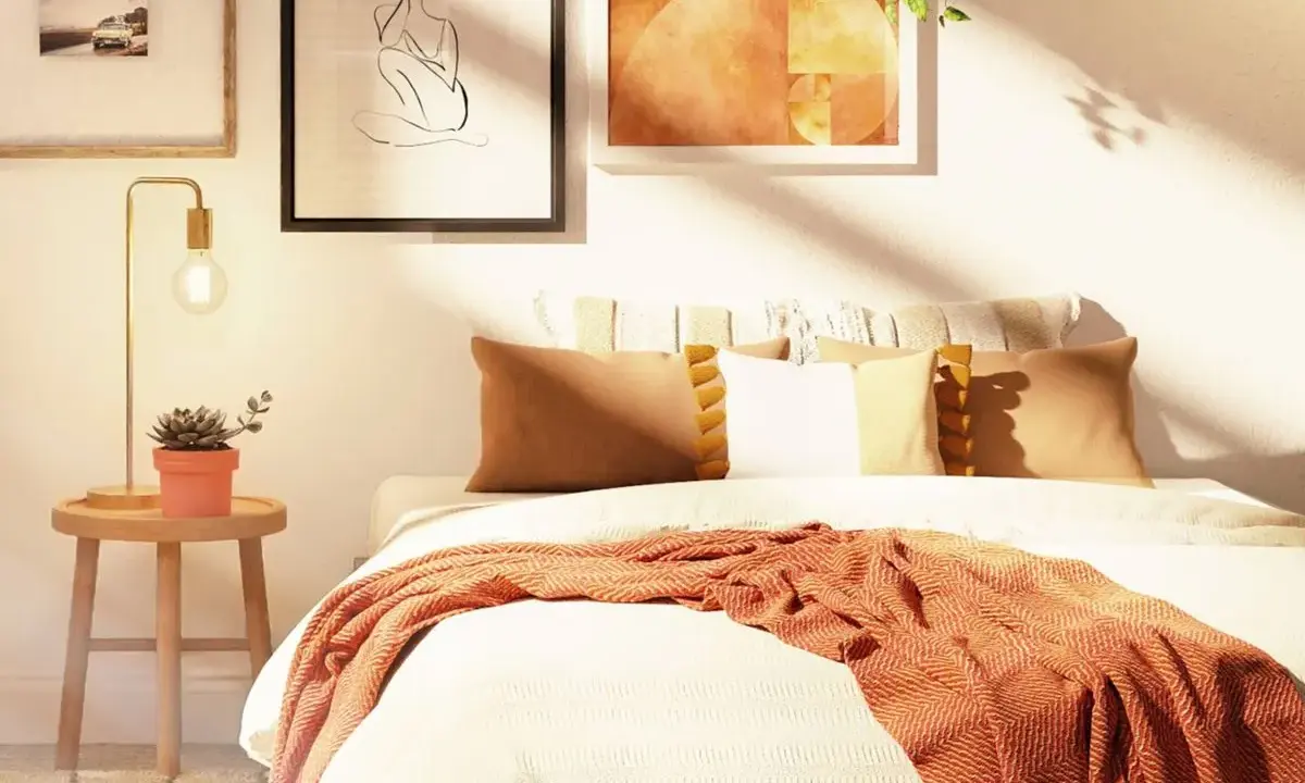 Acogedora habitación con decoración nórdica, cama con mantas y cojines cálidos, mesita de noche con planta y lámpara, y cuadros en la pared.