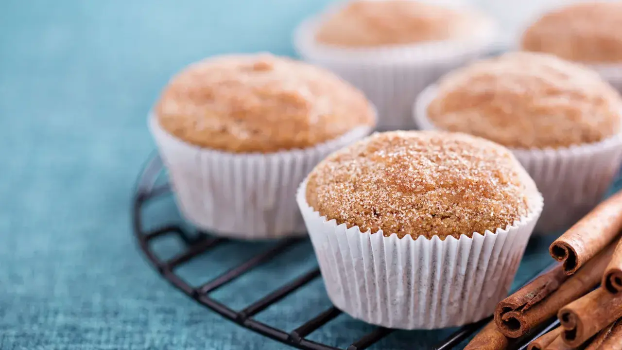 Leckere Apfelmus Muffins mit Zimt bestreut auf einem Gitter, daneben Zimtstangen.