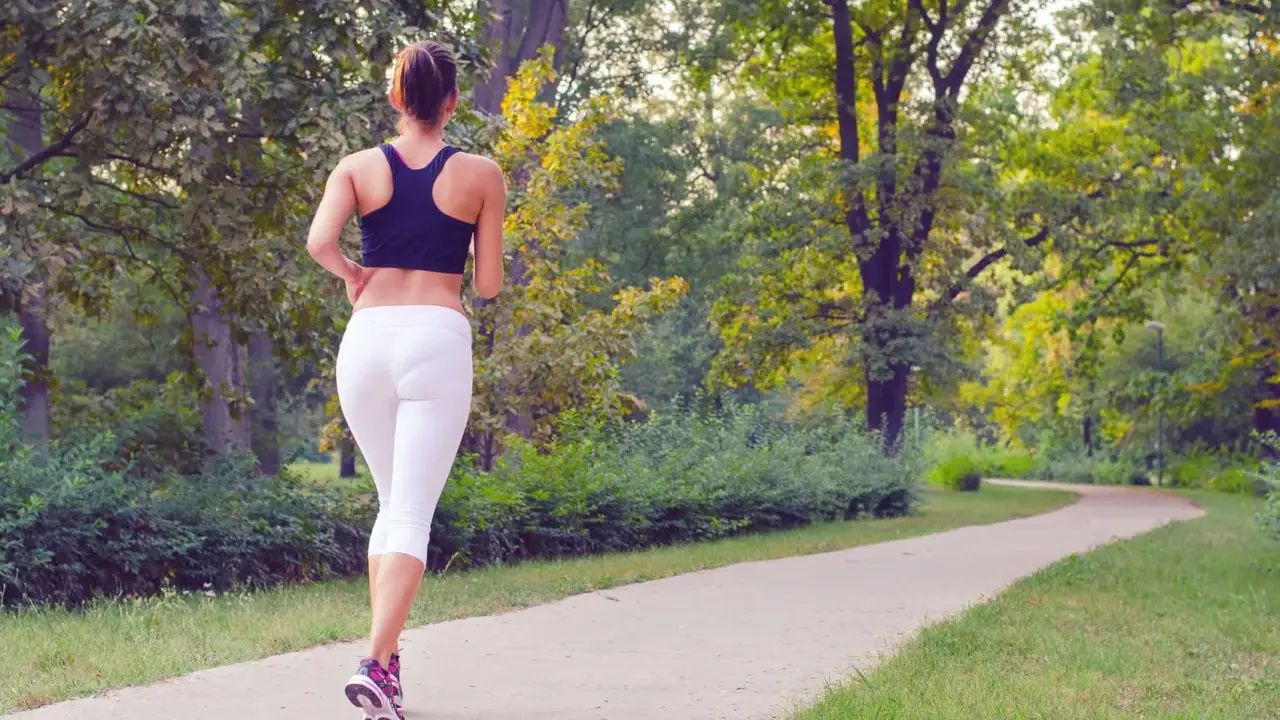 Donna corre su un sentiero nel parco, godendosi la sua zona 2 corsa tra gli alberi verdi.