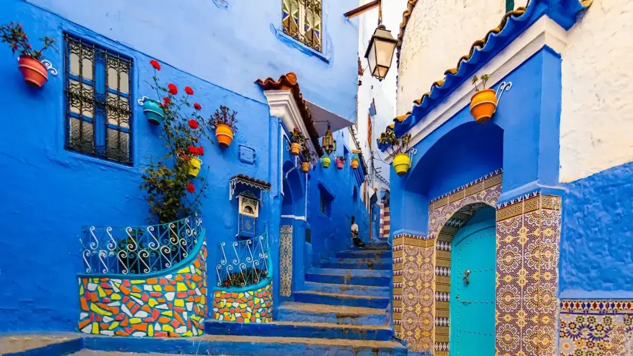 Maroko gdzie na wakacje? Urokliwa, niebieska uliczka w Chefchaouen z kolorowymi doniczkami i mozaikami zaprasza do odkrywania.