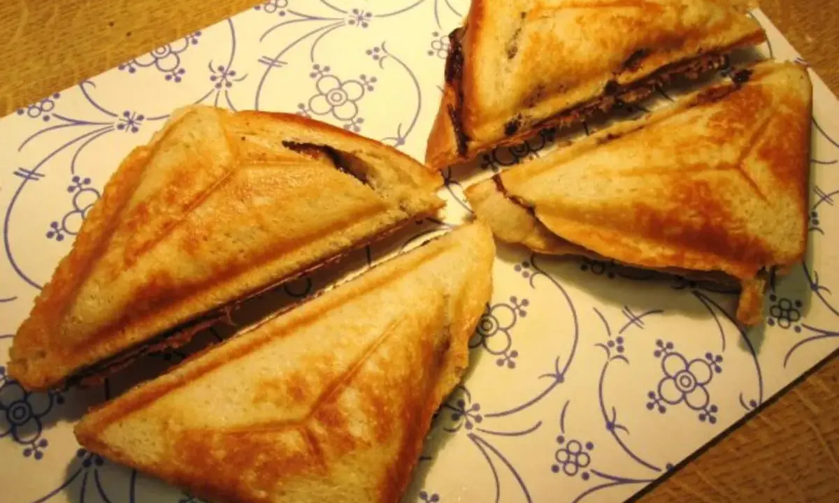 Goldbraune Bananen-Toast-Sandwiches, dreieckig geschnitten, liegen auf einem Teller mit blau-weißem Muster.