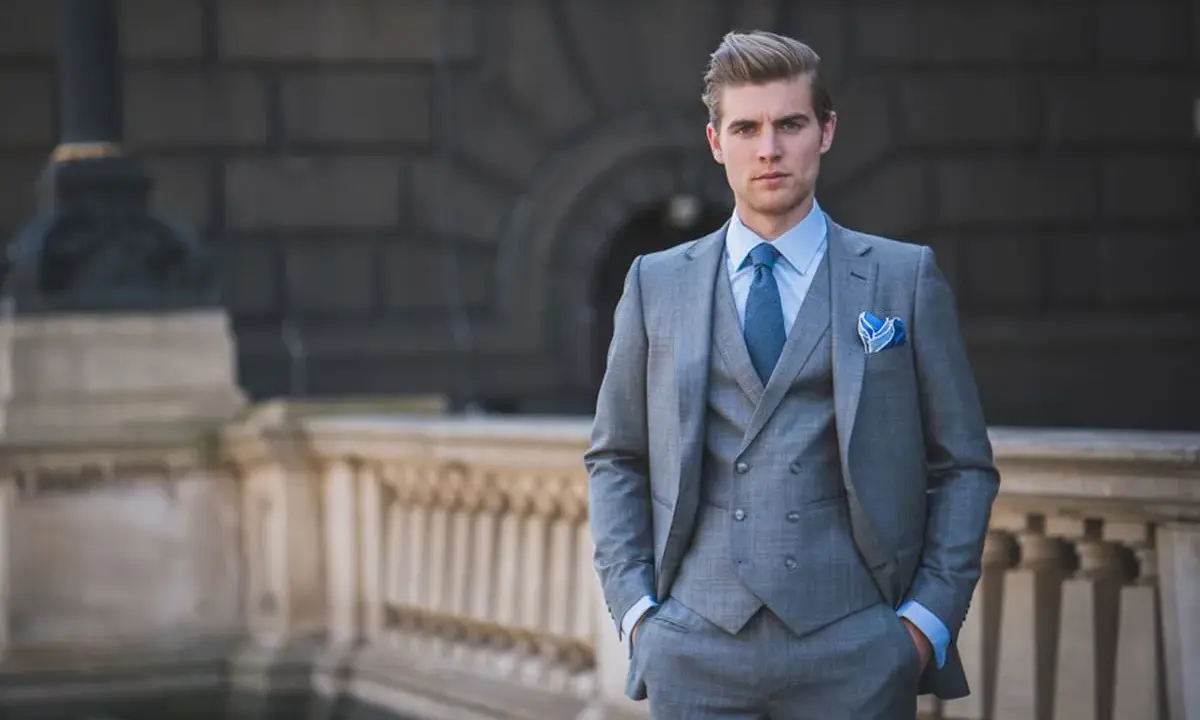A man in a sharp grey suit, vest, and blue tie exemplifies formal cocktail attire for men, ready for any elegant event.
