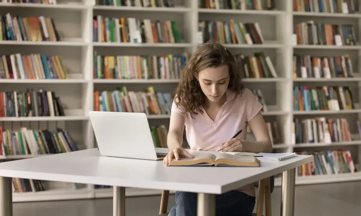 Młoda kobieta uczy się w bibliotece, zastanawiając się, czy studia chemiczne to dobry wybór.