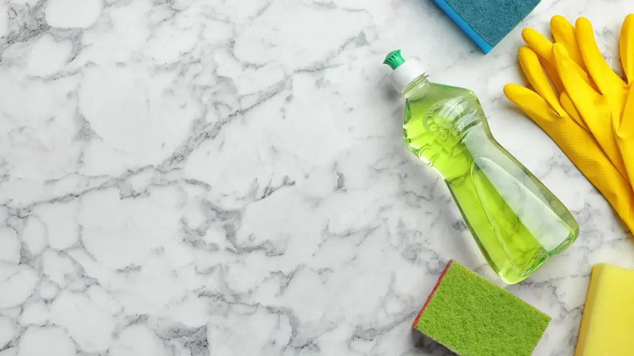 Reinigungsutensilien wie Spülmittel, Handschuhe und Schwämme liegen bereit, um Marmor zu reinigen.