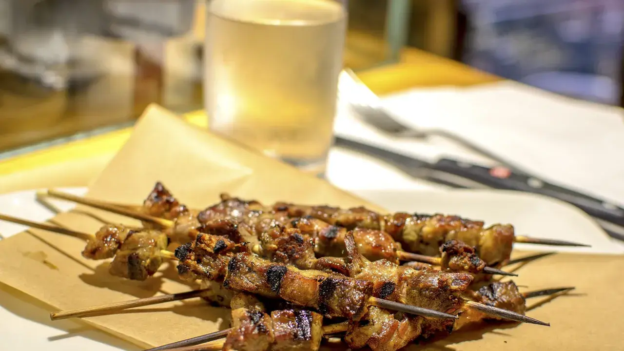 Arrosticini, uno dei piatti tipici abruzzesi, serviti su carta paglia con un bicchiere di vino bianco sullo sfondo.