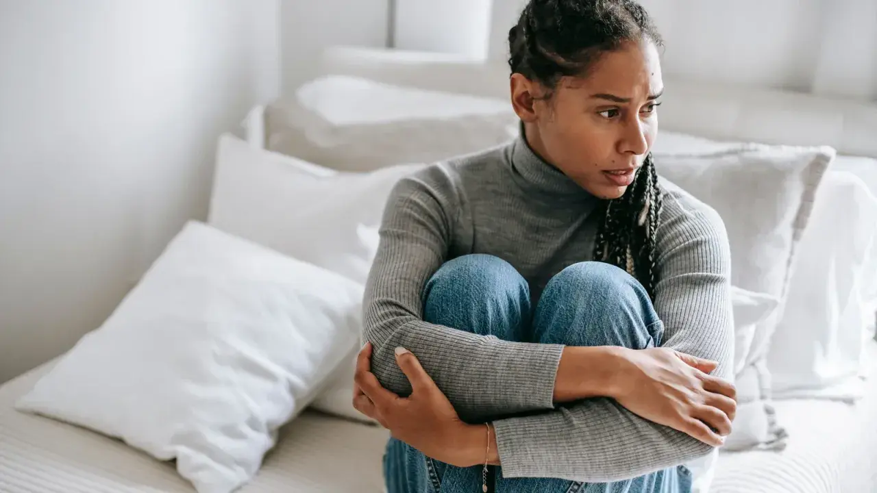 Donna seduta sul letto, abbracciata, con espressione preoccupata. Sembra soffrire di ansia da separazione dal partner.