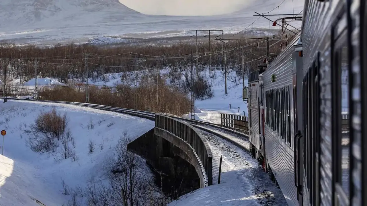 Tåg luleå narvik färdas genom ett snöigt landskap med berg i bakgrunden.