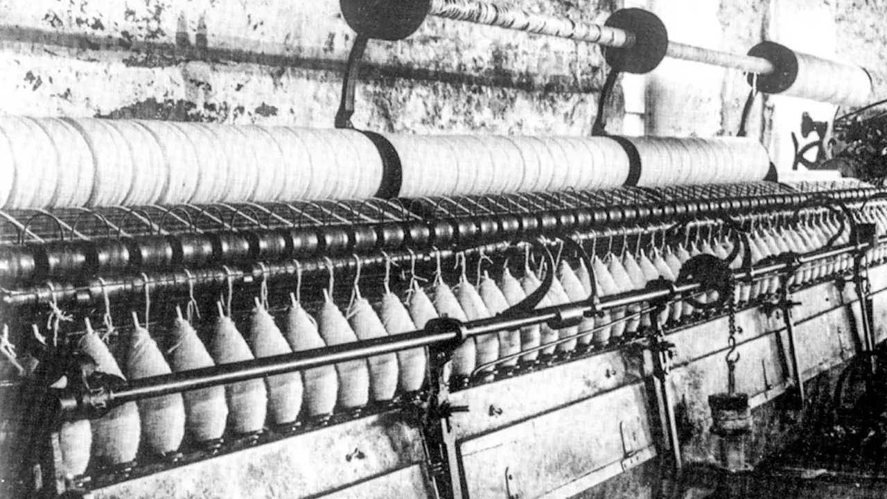 Macchinario industriale per la filatura con fili avvolti su bobine e grandi rulli.