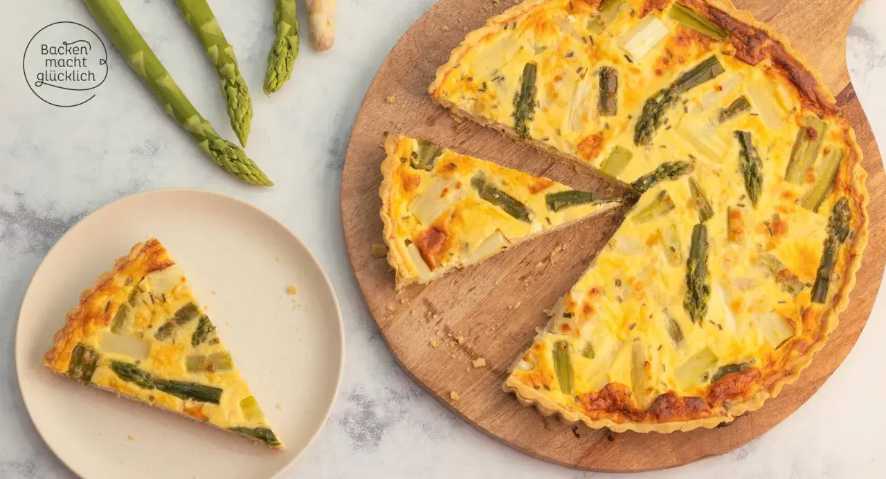 Herzhafte Spargel Quiche mit frischem Spargel, goldbraun gebacken. Ein Stück auf einem Teller, der Rest auf einem Holzbrett.