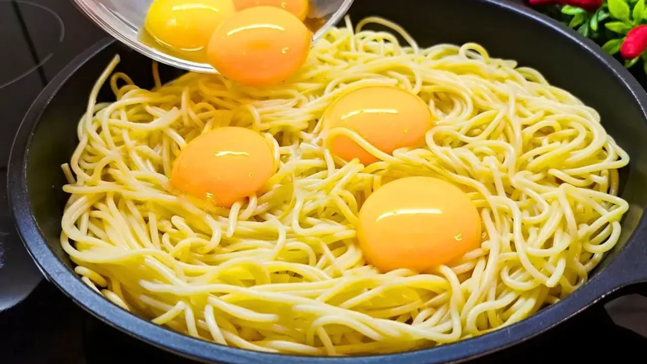 Makaron z jajkiem w patelni, żółtka tworzą złote kropki na żółtym tle.