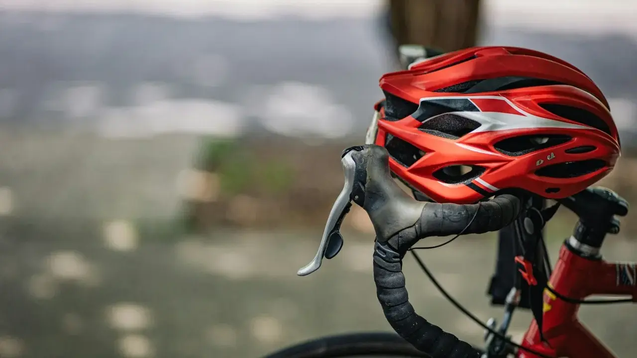 Czerwony kask rowerowy i kierownica z owijką. Niezbędne wyposażenie rowerzysty na bezpieczną podróż.