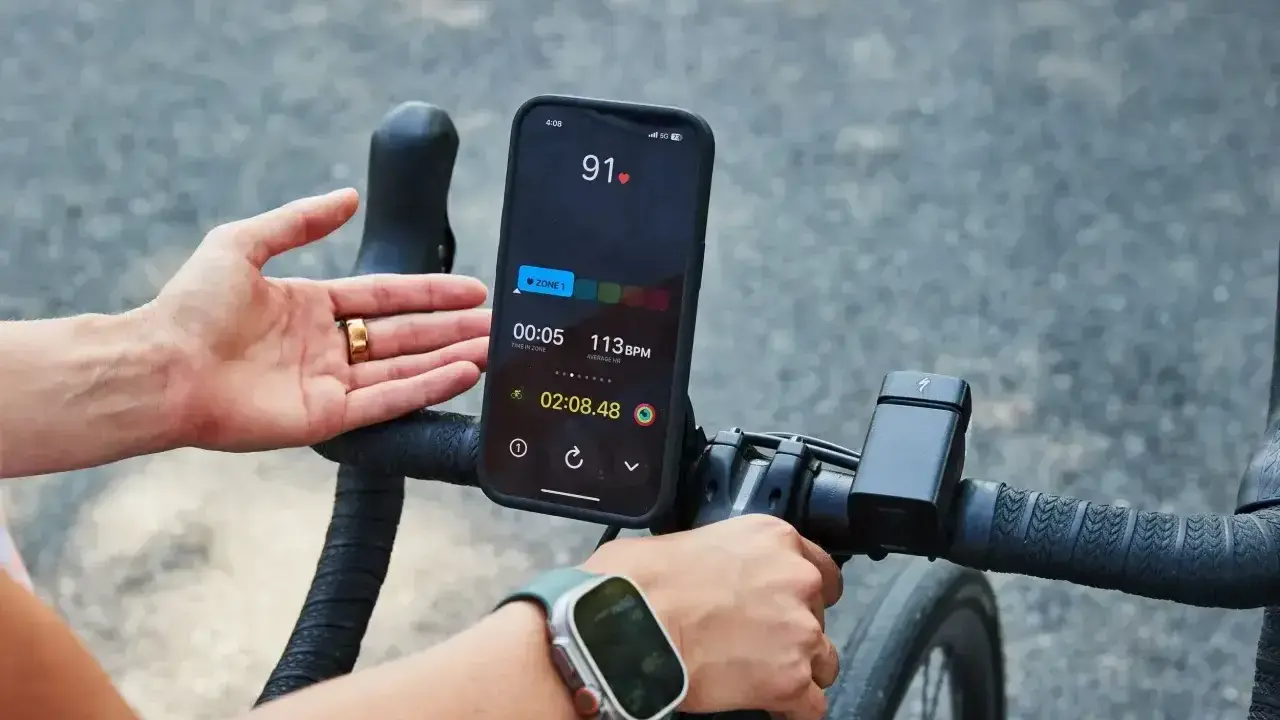 Rowerzysta sprawdza na telefonie, co oznacza puls 91. Na ekranie widać tętno 113 BPM i czas treningu.