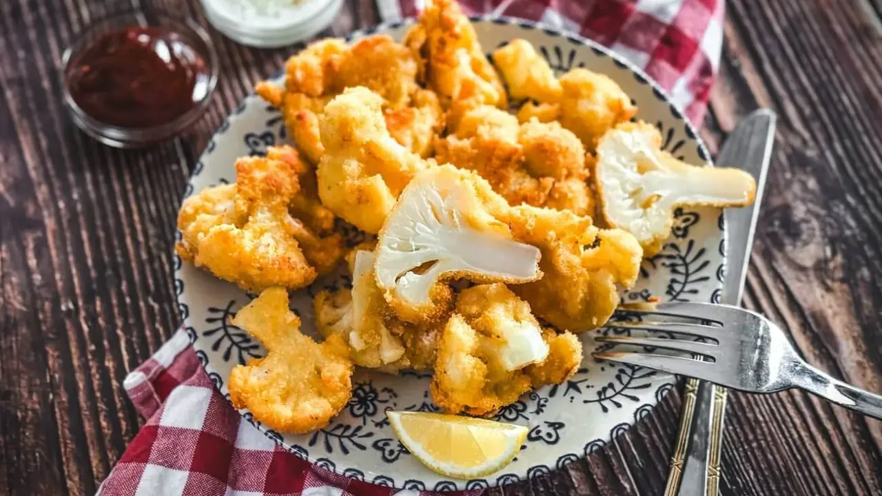 Knusprig panierter Blumenkohl, eine köstliche low carb Alternative zu Pommes. Serviert mit Dips und Zitrone auf einem Holztisch.