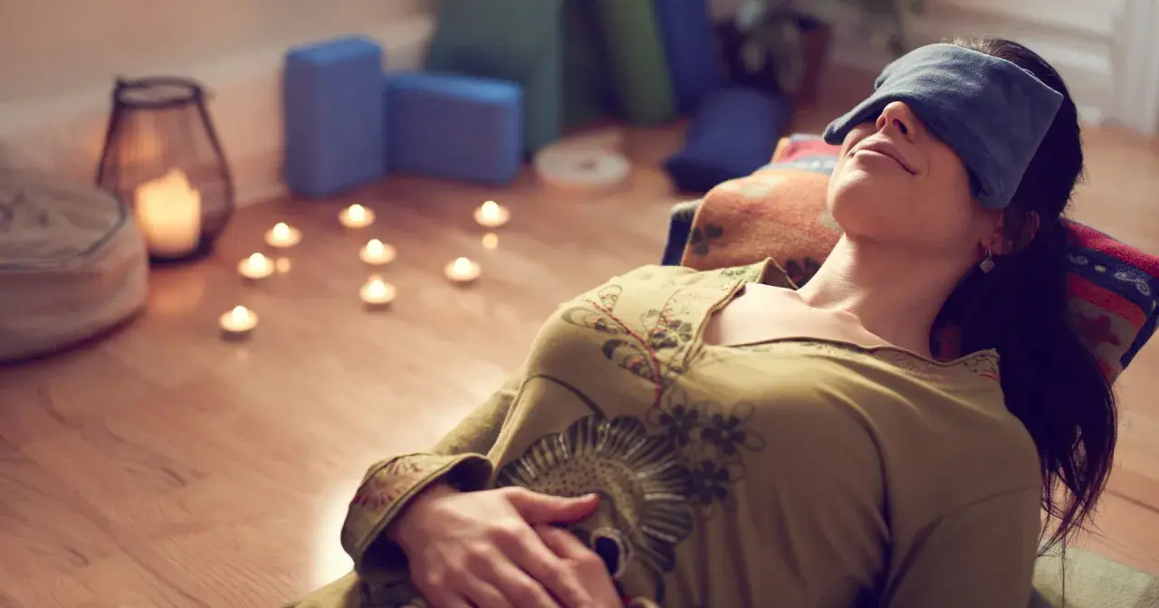 Kvinna med ögonbindel vilar under brahma yoga, omgiven av levande ljus och yogablock.
