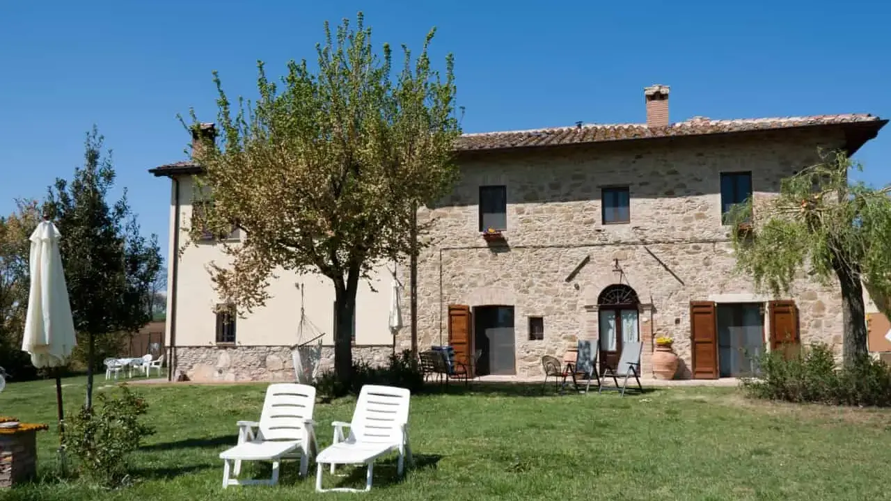 Un casale in pietra con giardino e lettini, perfetto per vacanze tranquille ad agosto in Italia.