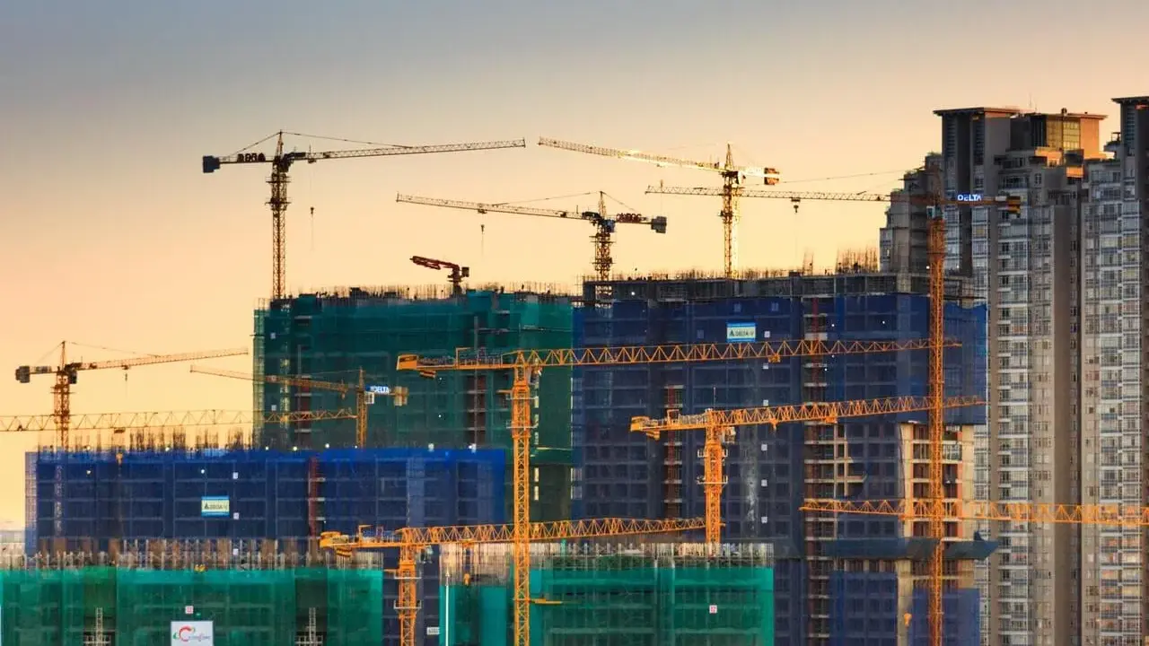 Grúas de construcción trabajando en la edificación de rascacielos, mostrando los elementos estructurales de un edificio en proceso.