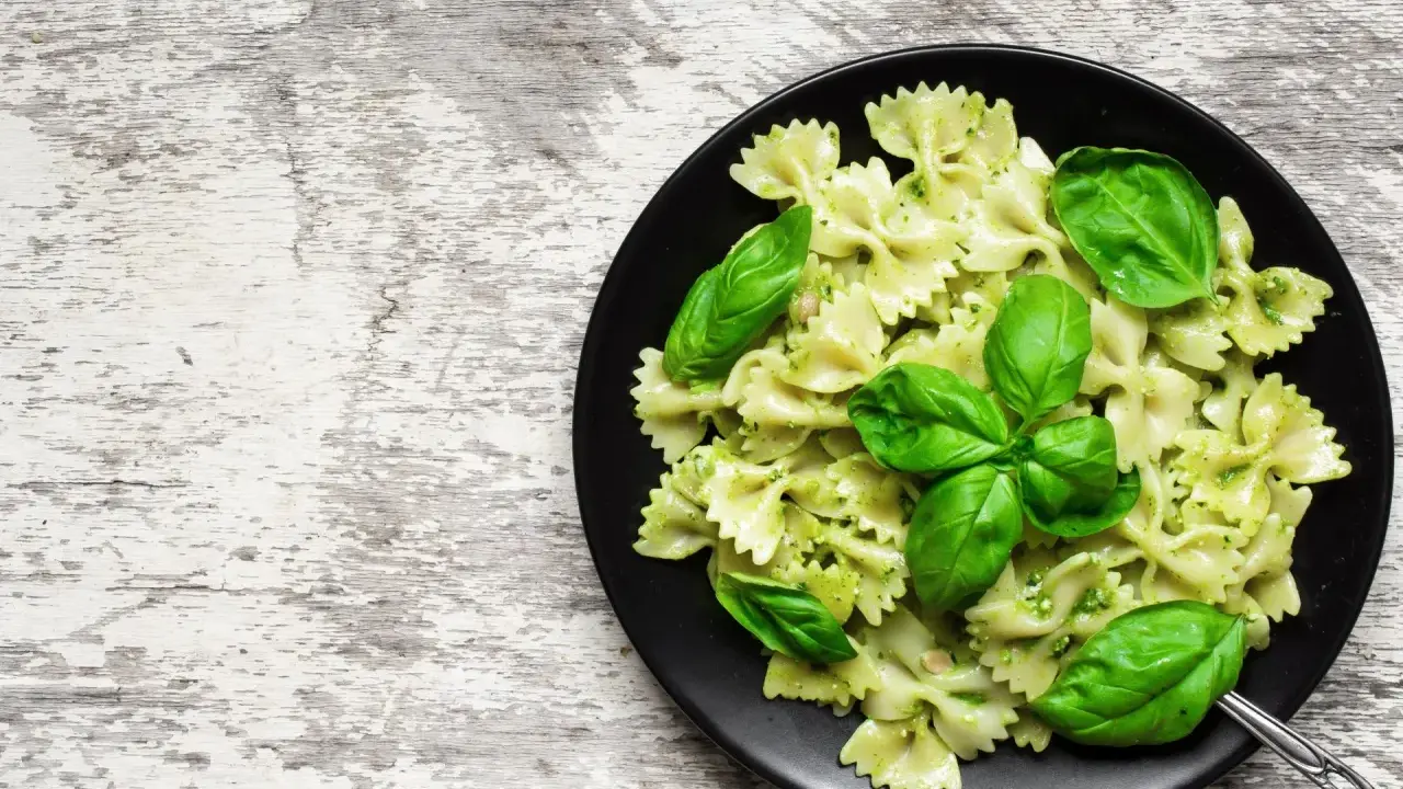Lekkostrawny makaron farfalle z pesto i świeżą bazylią na czarnym talerzu, gotowy do podania.