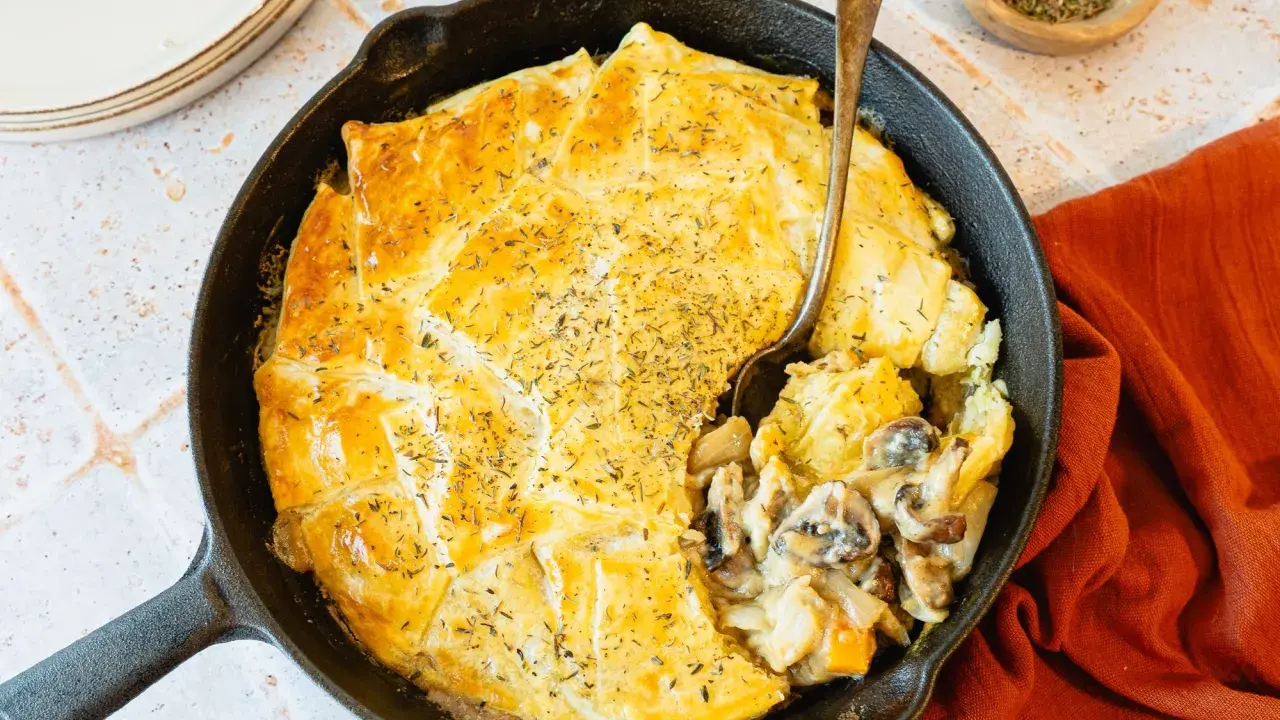 Une tourte aux champignons dorée et appétissante, servie dans une poêle en fonte, avec une cuillère prête à déguster.
