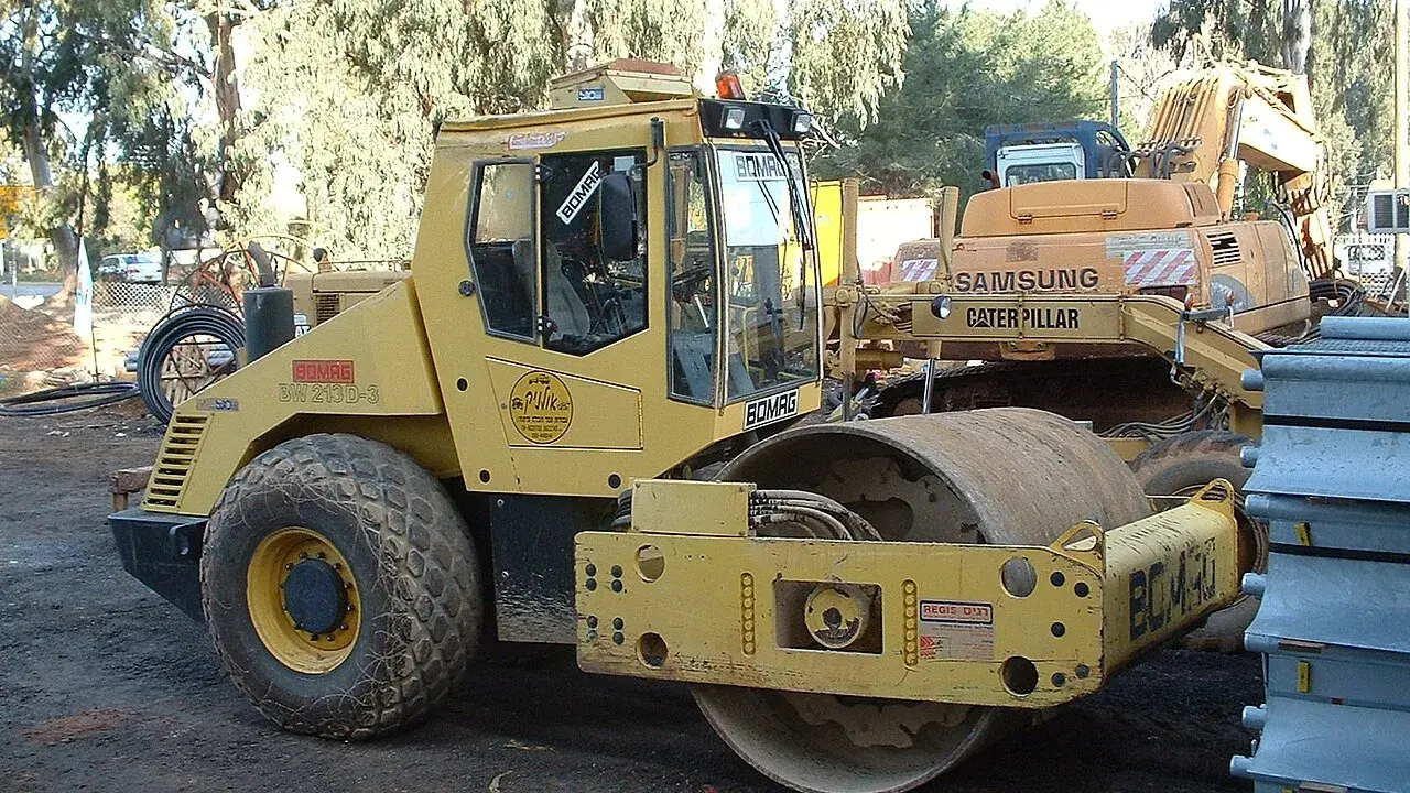 Żółty walec drogowy BOMAG BW 213D-3 na placu budowy, obok koparki Samsung Caterpillar.