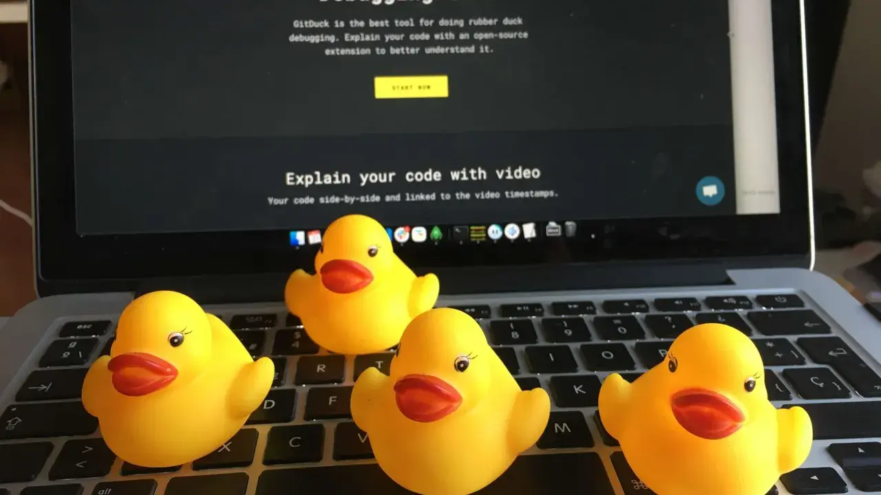 Cztery żółte gumowe kaczuszki siedzą na klawiaturze laptopa, obok ekranu z napisem "The Rubber Duck Debugging tool".