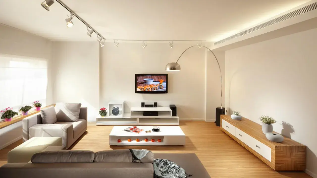 Un salón moderno con sofás grises, mesa de centro blanca y TV. La iluminación, con focos en riel y lámpara de arco, es clave para como iluminar un salón.