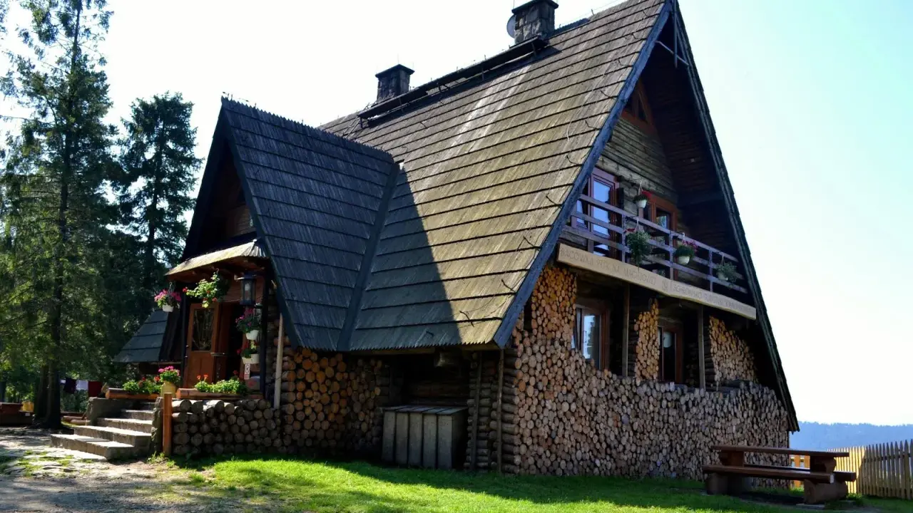 Drewniana bacówka na Turbaczu, z kamiennymi schodami i stosem drewna. Stare wierchy zapraszają do odpoczynku.