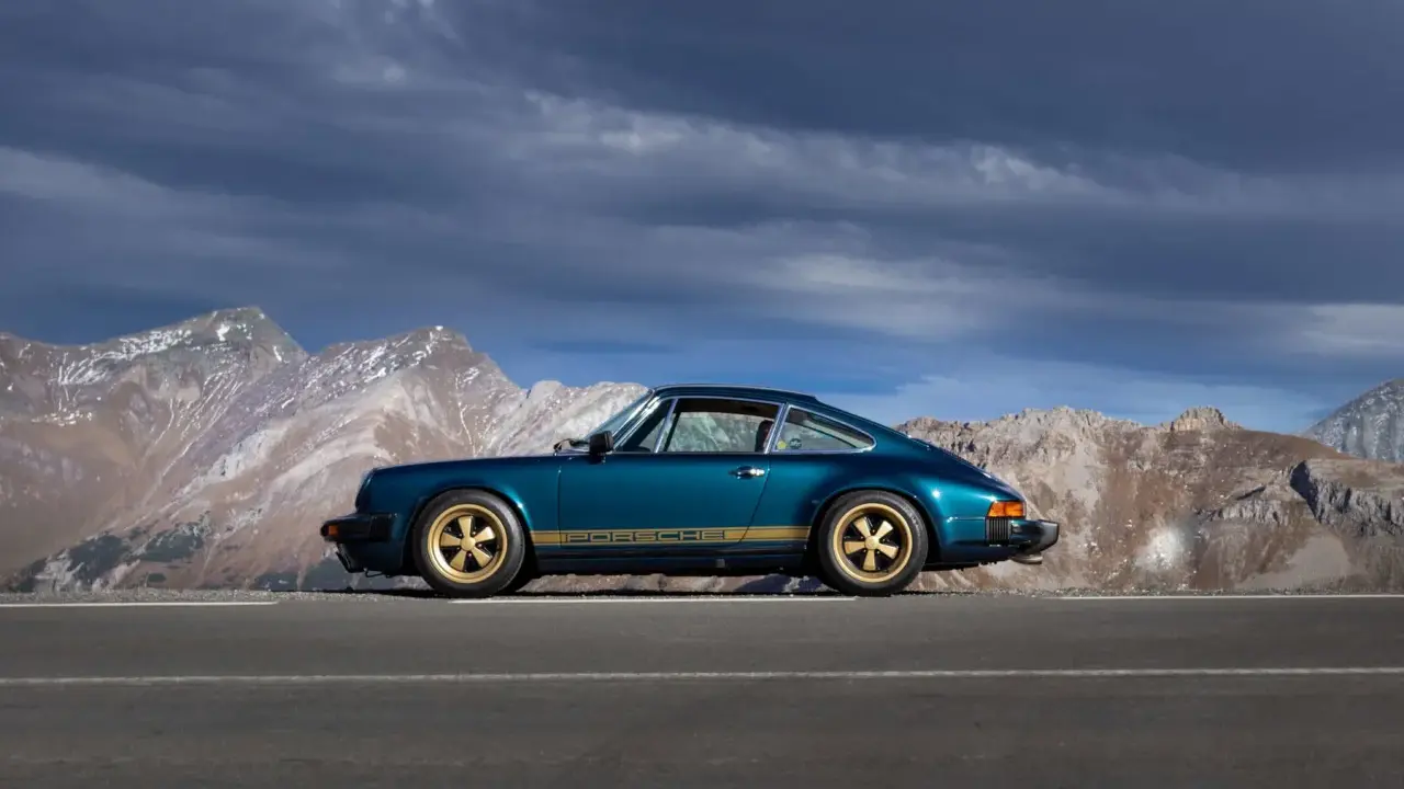 Ein türkisfarbener Porsche 911 SC mit goldenen Felgen und Streifen steht auf einer Bergstraße. Die Wertentwicklung dieses Klassikers ist beeindruckend.