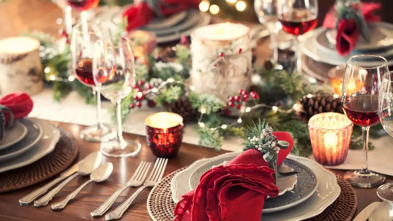 Tavola apparecchiata per un magico pranzo di Natale, con candele, pigne e luci scintillanti. Dove andare per un'atmosfera così?