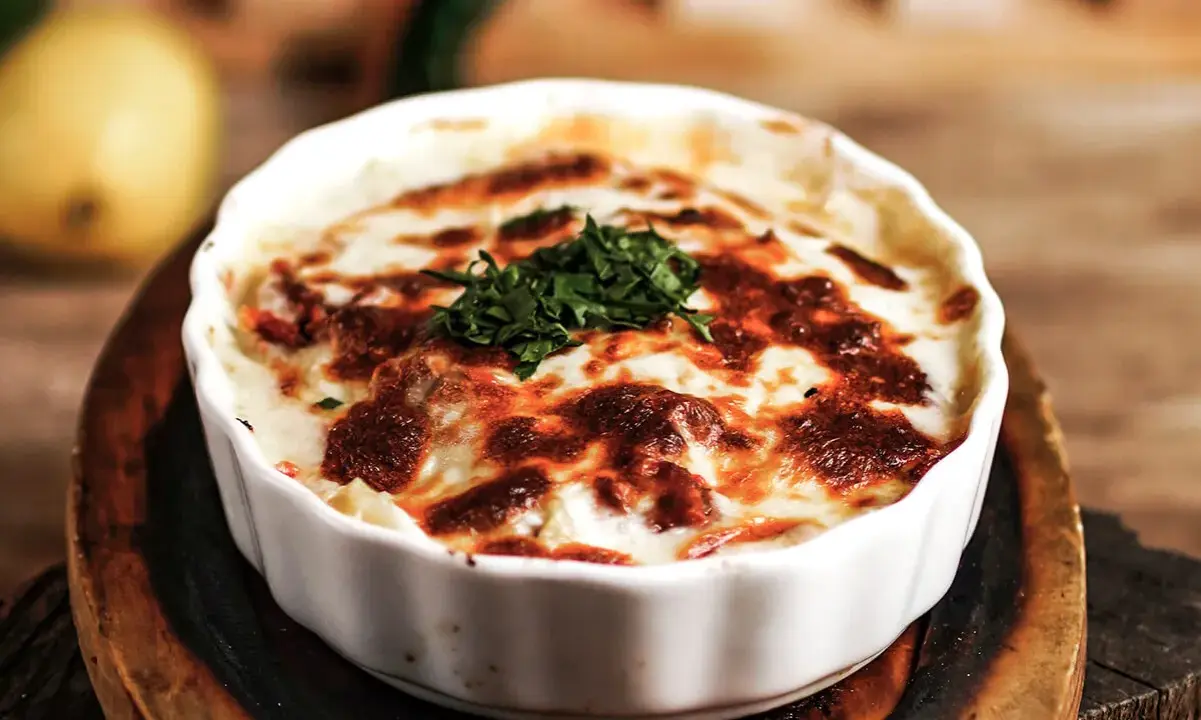 En krämig lasagne vegetarisk med gyllene ost och färska örter, serverad i en vit ugnsform.