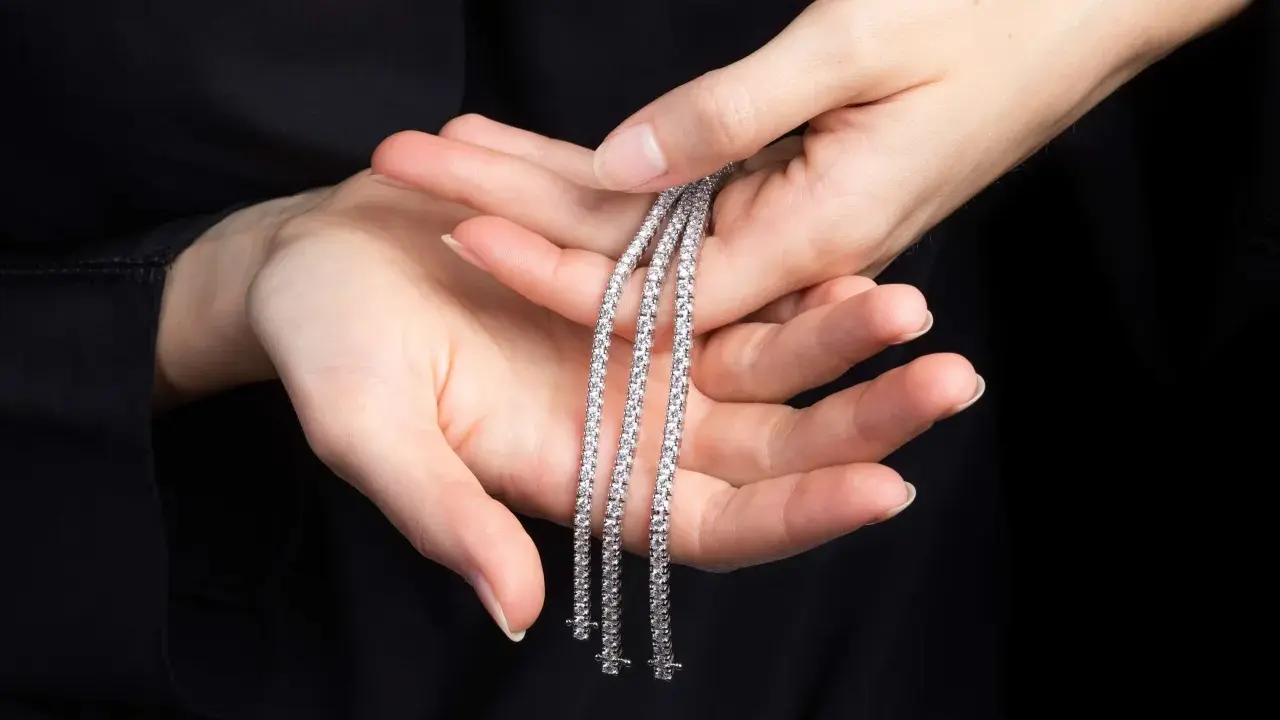Mani delicate tengono tre scintillanti bracciali tennis, un classico intramontabile la cui storia affonda le radici nel mondo dello sport.