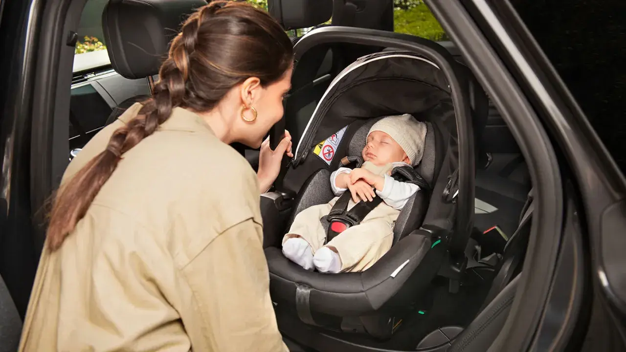 Madre mira a su bebé dormido en la silla coche, asegurando la correcta postura recien nacido silla coche para un viaje seguro.
