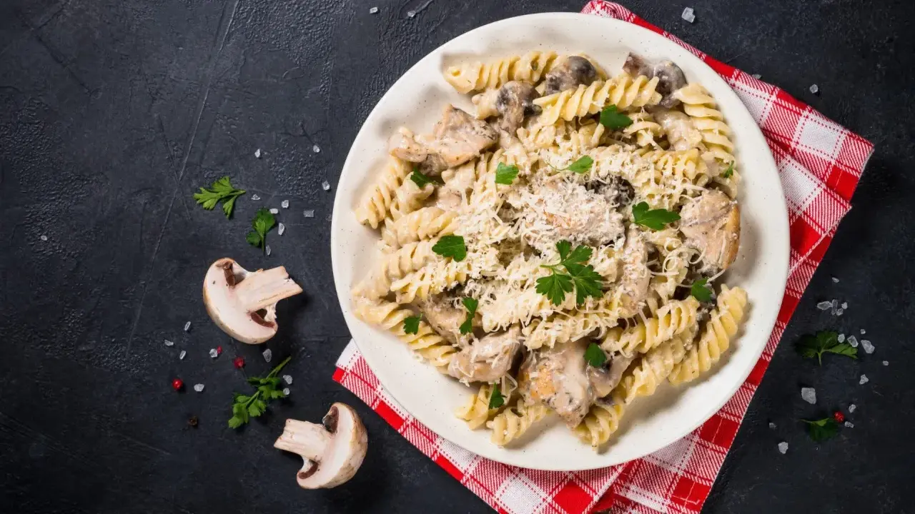 Pyszny makaron z kurczakiem i pieczarkami w kremowym sosie, posypany parmezanem i świeżą pietruszką.